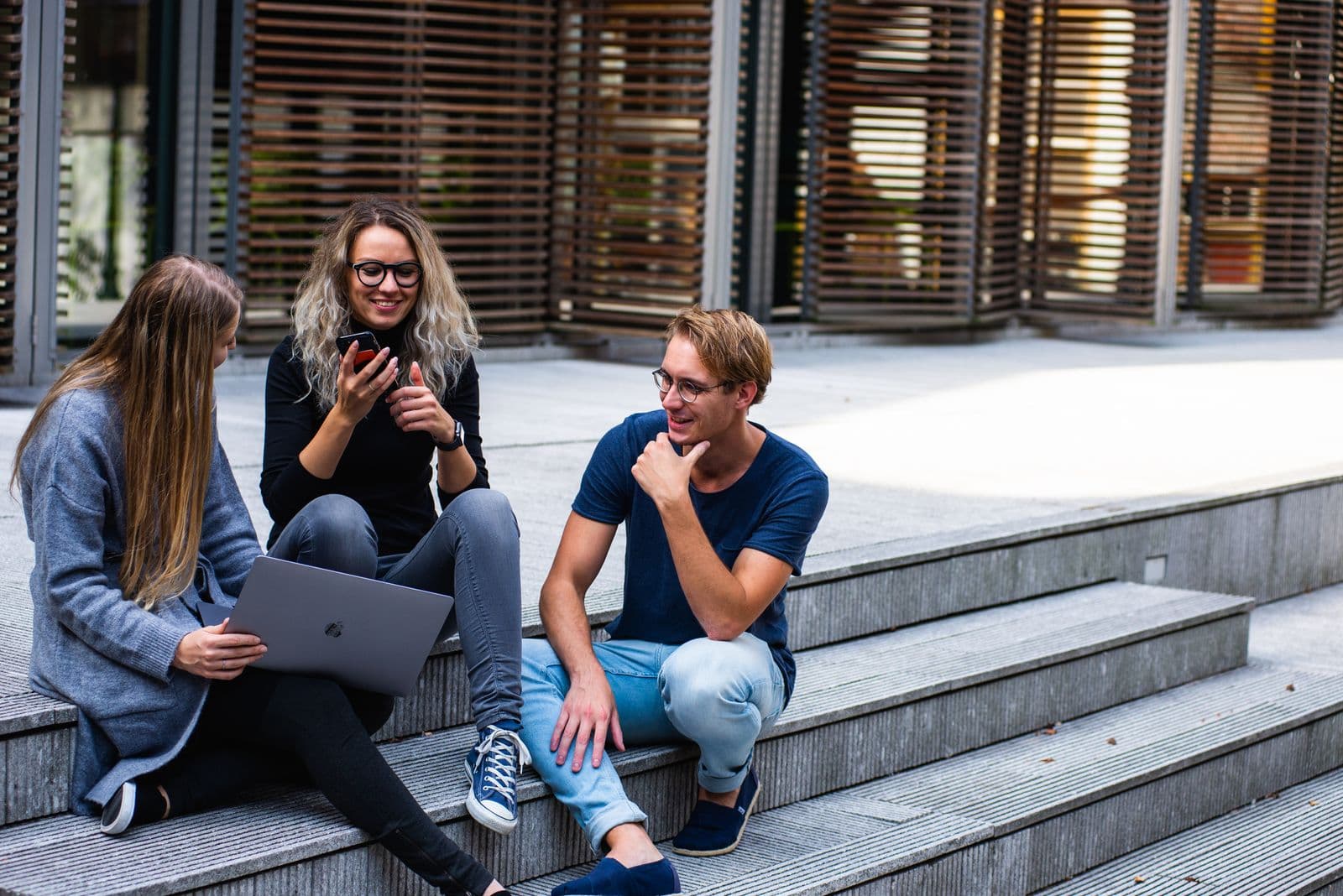 Students collaborating with a laptop on a campus plaza
